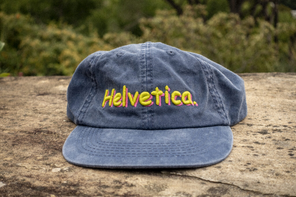 Faded navy dad cap displaying the word "Helvetica" in the Comic Sans font. New cap, funny cap, camper cap, washed cotton, Irony, Humor, meme, Brass clasp.