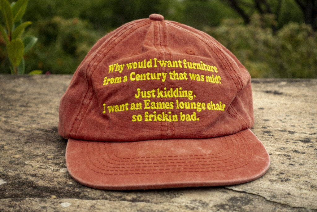Faded burnt orange dad cap displaying the text, "Why would I want furniture from a century that was mid? Just Kidding. I want an Eames lounge chair so frickin bad." New cap, funny cap, camper cap, washed cotton, Irony, Humor, meme, Brass clasp.